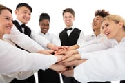 A smiling group of restaurant workers stand in a circle, each with one hand extended to the middle of the circle.