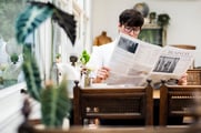 A man wearing glasses reads the business section of a newspaper sitting in a restaurant.